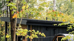 A modern, black wooden cabin with a circular window, surrounded by lush greenery and trees. - Private Sauna + Fireplace · Wildernest Cabins #3 (Duluth)