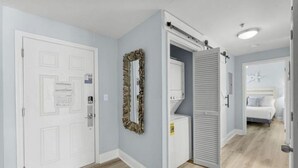 A hallway with a white door, a mirror, and a bed in the adjacent room. - Bright & Stylish Condo Near Everything! (Panama City Beach)