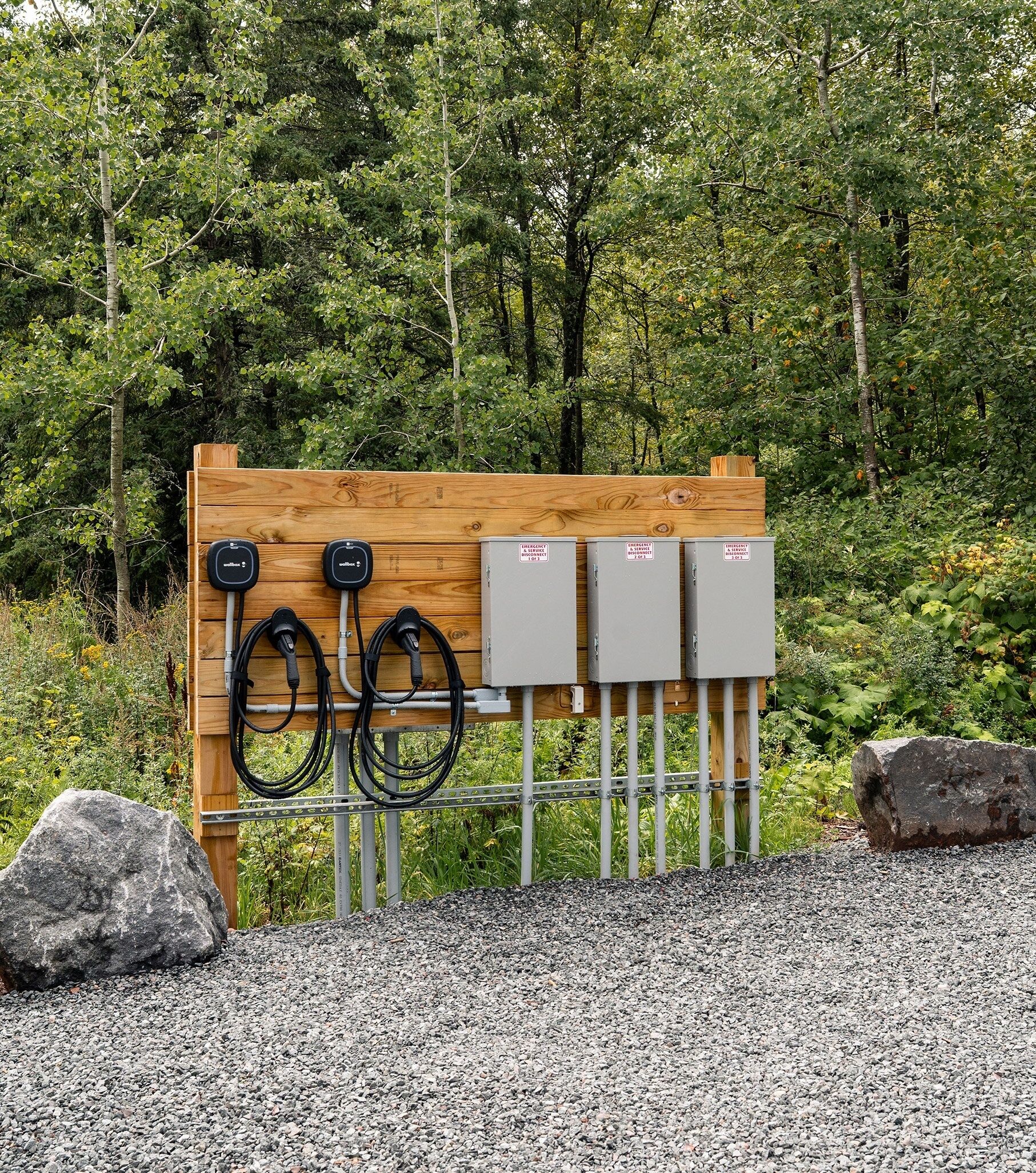 A wooden utility board with two black charging stations and three grey electrical boxes.