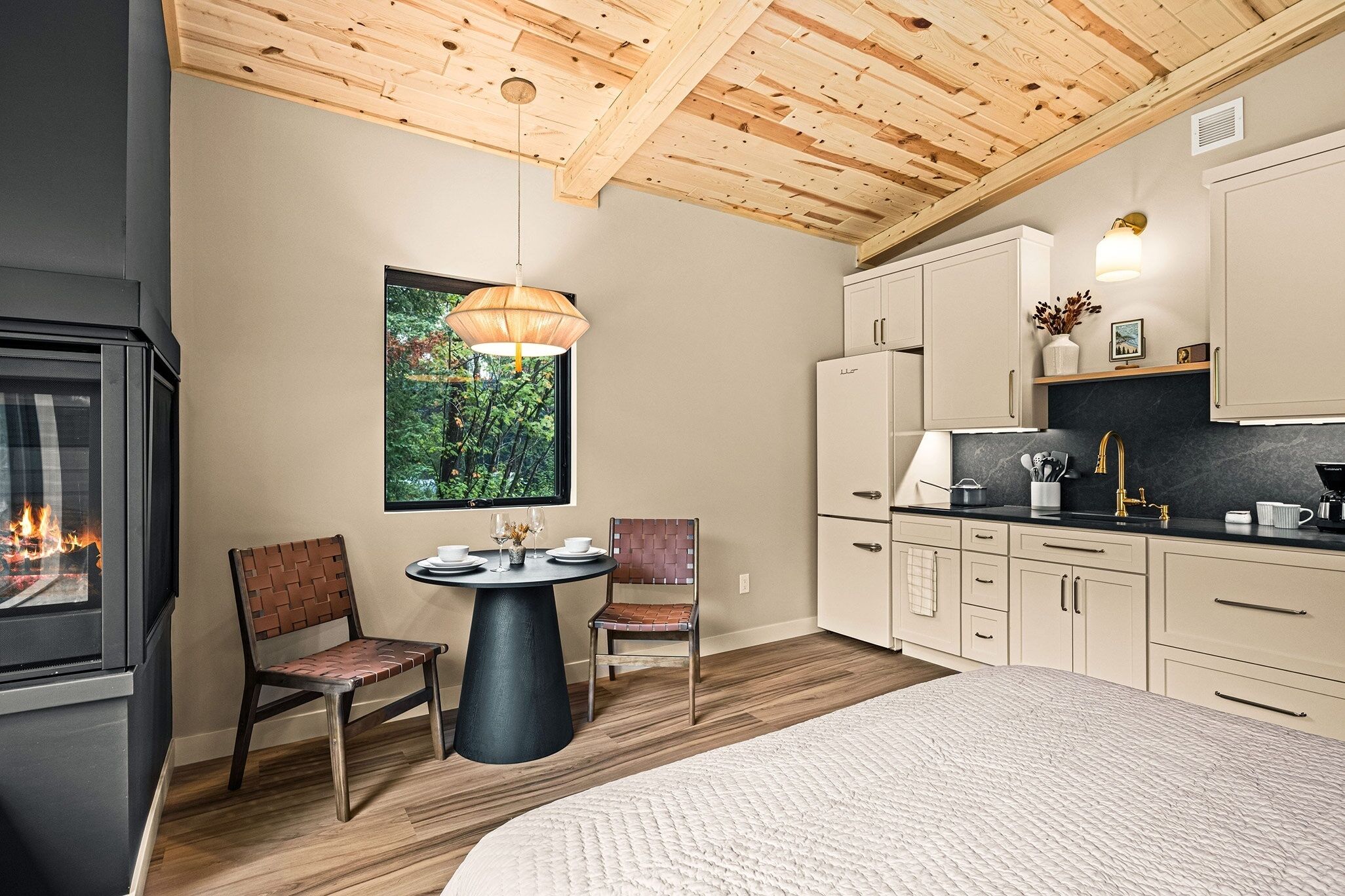 Een gezellige kamer met een open haard, een eettafel met stoelen, een bed en een keuken met kasten en een aanrecht.