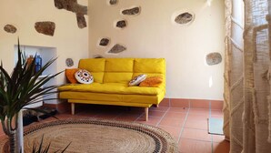 Un canapé jaune agrémenté de coussins à motifs, un tapis tissé et un mur décoré d’éléments rappelant la pierre.