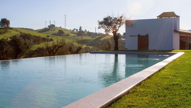 Une piscine offrant une vue dégagée sur le paysage environnant, notamment une colline et un bâtiment doté d’un toit plat.