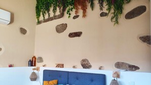 Une chambre avec un lit bleu, des coussins décoratifs, un climatiseur fixé au mur et une étagère contenant divers objets.