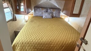 A bed with a quilted cover, wooden headboard, and a skylight above. - Rv with 1 Bedrooms, and sofa bed Full Kitchen, Dining Area & Modern Bathroom” (Pikeville)