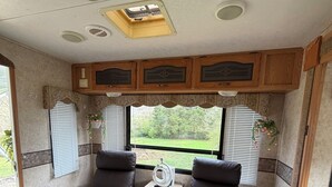 A cozy RV interior with two reclining chairs, a small table with a decorative item, and a window with blinds. - Rv with 1 Bedrooms, and sofa bed Full Kitchen, Dining Area & Modern Bathroom” (Pikeville)