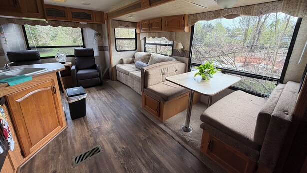 A well-equipped RV interior with a kitchenette, seating area, and large windows offering a view of the outdoors. - Rv with 1 Bedrooms, and sofa bed Full Kitchen, Dining Area & Modern Bathroom” (Pikeville)