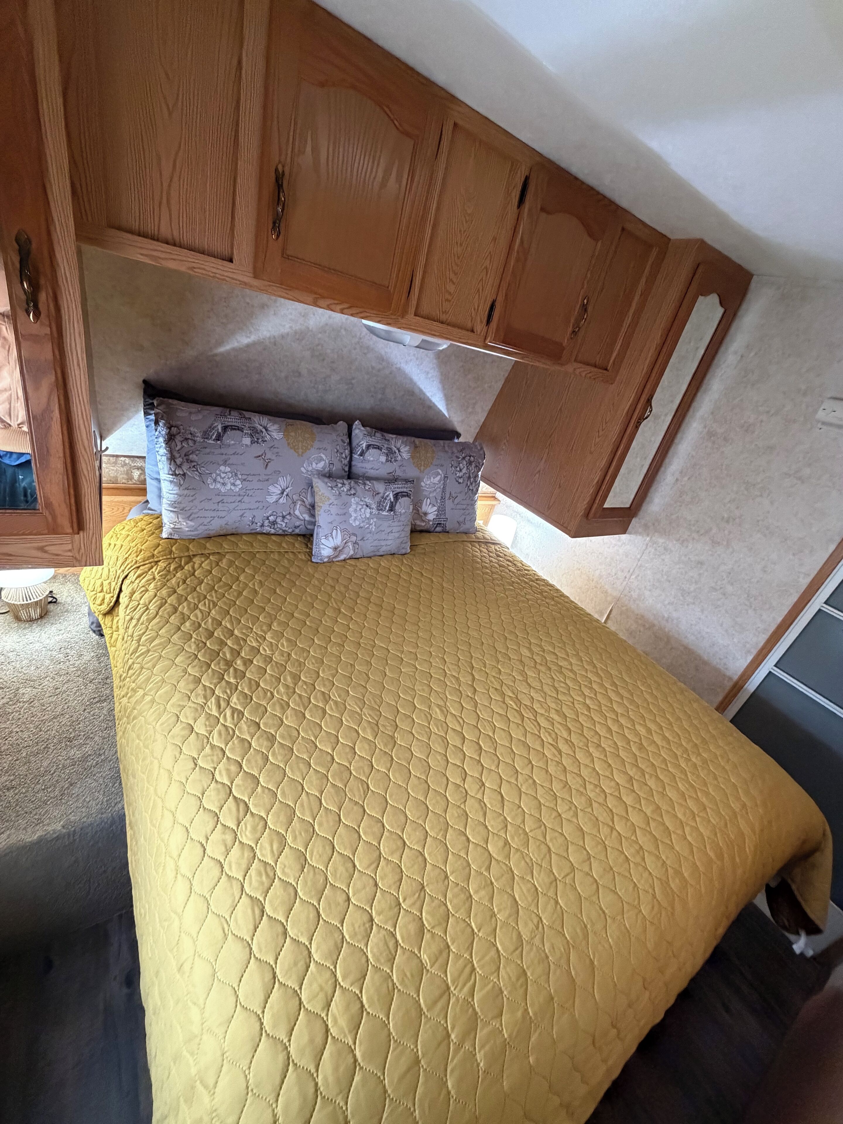 A bed with a quilted yellow cover, wooden headboard, and decorative pillows.