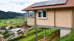 A house with a balcony, solar panels, and a view of a green valley. - Apartment 'Panoramahisli 4' with Mountain View, Balcony and Air Conditioning (Fischerbach)