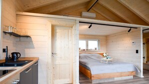 A wooden cabin interior with a kitchen, a bed, and a window. - Apartment 'Panoramahisli 4' with Mountain View, Balcony and Air Conditioning (Fischerbach)