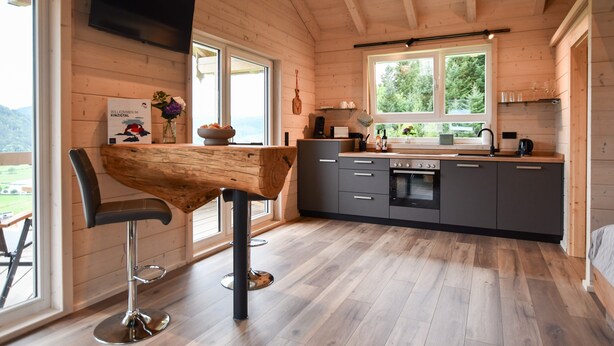 A modern kitchen with wooden walls, a bar stool, a TV, and a large window. - Apartment 'Panoramahisli 4' with Mountain View, Balcony and Air Conditioning (Fischerbach)