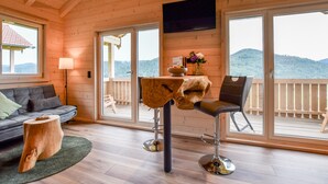 A wooden interior with a sofa, a table with a unique wooden top, a bar stool, and a TV mounted on the wall. - Apartment 'Panoramahisli 4' with Mountain View, Balcony and Air Conditioning (Fischerbach)
