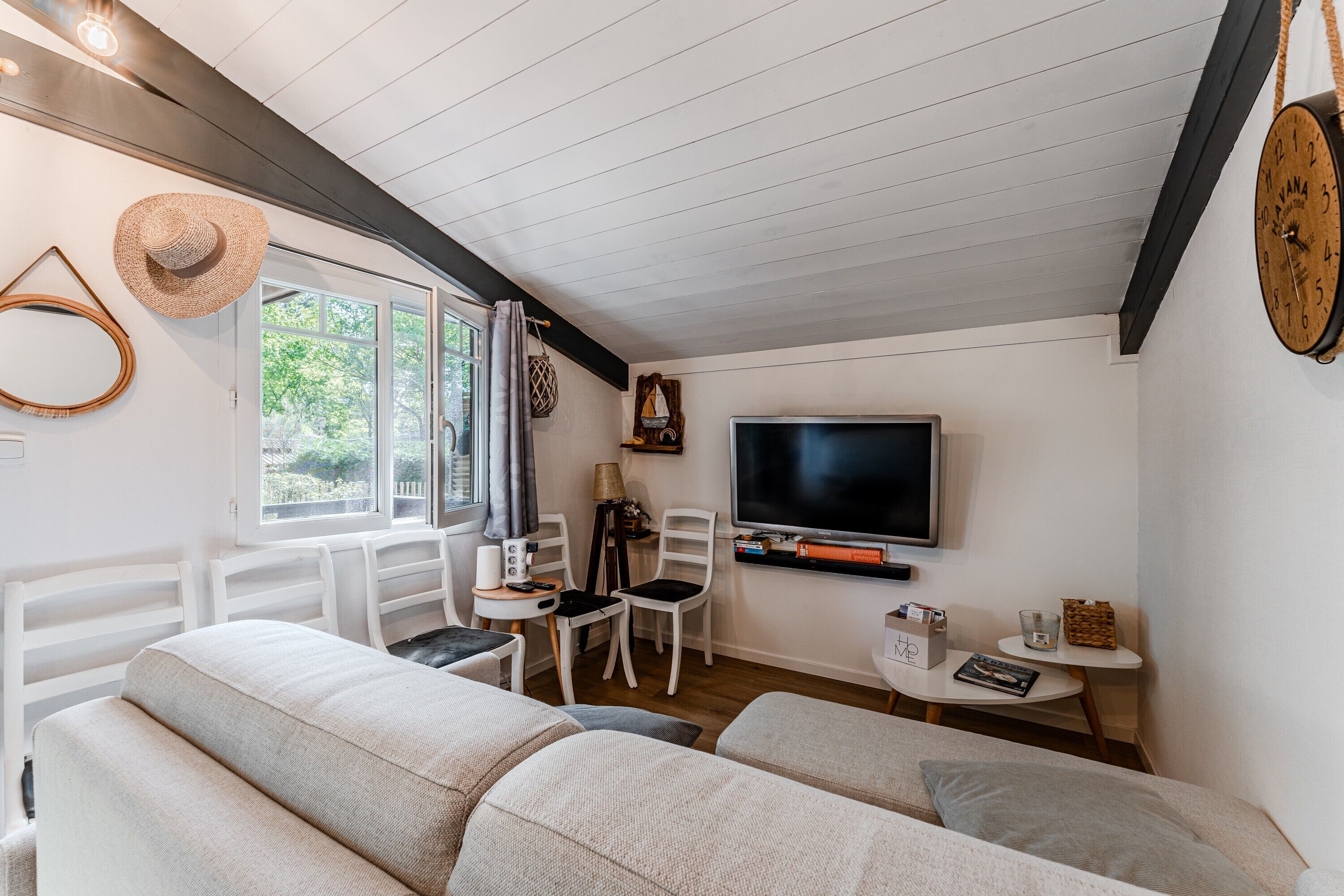 A cozy living room with a TV, white furniture, and a large window.