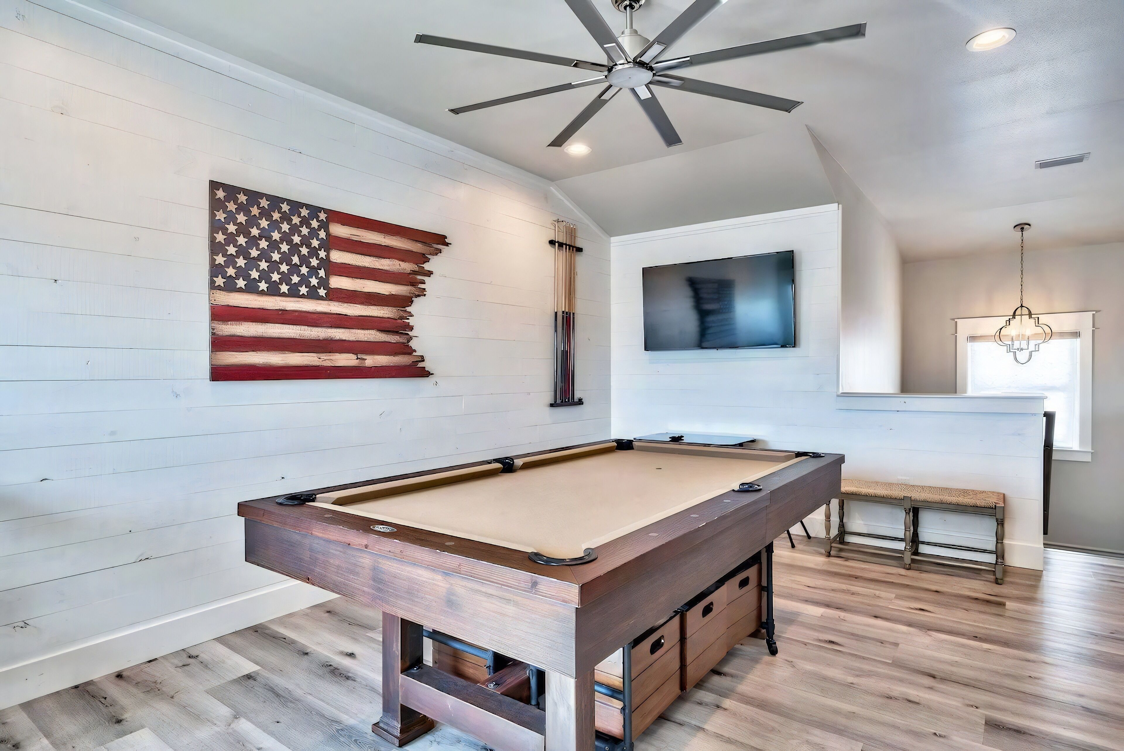 Een pooltafel in een kamer met houten vloeren, een plafondventilator en een geplakte Amerikaanse vlag.