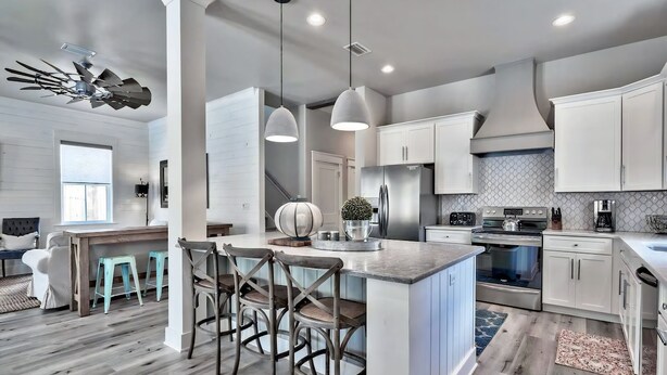 A modern kitchen with white cabinets, a central island with stools, a large stove, and a ceiling fan. - King's Castle | Luxury Beach Escape | Huge Private Pool/Spa | 6-Seater Golf Cart (Destin)
