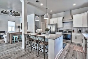 A modern kitchen with white cabinets, a central island with stools, a large stove, and a ceiling fan. - King's Castle | Luxury Beach Escape | Huge Private Pool/Spa | 6-Seater Golf Cart (Destin)