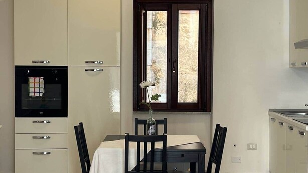 A compact kitchen with a dining table, chairs, a window, and built-in appliances. - Arte 36 (Bosa)