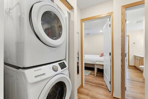 Ein Waschbereich mit gestapelten Waschmaschinen und ein Schlafzimmer mit Bett, Nachttisch und Holzboden.