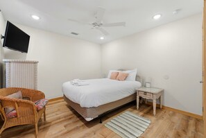 Ein Schlafzimmer mit einem Bett, einem Sessel, einem Nachttisch, einem Fernseher und einem Deckenventilator.