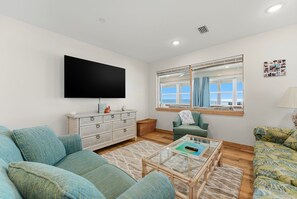 Ein Wohnzimmer mit Flachbildfernseher, einer Couch, einem Sessel, einem Couchtisch und einem Fenster mit Aussicht.