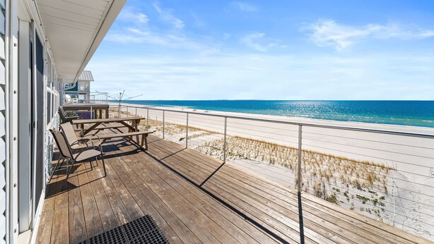 Eine Holzterrasse mit Gartenmöbeln mit Blick auf einen Strand.