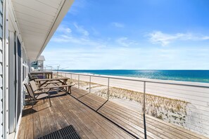 Une terrasse en bois, agréée de mobilier d’extérieur, donnant sur une plage.