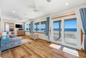 A room with a bed, a TV, a desk, and large windows with a beach view. - Stunning Beachfront Mexico Beach| 6 BR, Sleeps 18 (Mexico Beach)