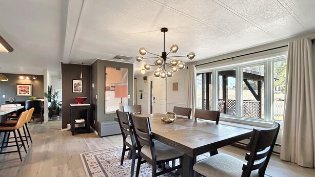 A dining area with a large table, chairs, and a chandelier. There is a kitchen area in the background with a countertop and chairs. - Walker Ridge Hideout Pets Pool Table (Montrose)