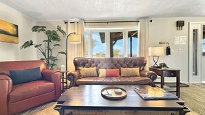 A living room with a brown leather sofa, a red armchair, a wooden coffee table, and a large window with curtains. - Walker Ridge Hideout Pets Pool Table (Montrose)