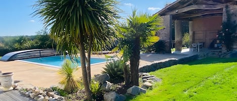 A pool area with a wooden deck, palm trees, and a stone wall.