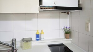 Et køkken med hvide skabe, en hane i rustfrit stål, et sort emfang og en urtepotte med lavendel på bordet.