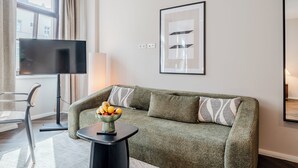 En moderne stue med en grøn sofa, et sofabord med frugt, et fladskærms-tv og et indrammet abstrakt kunstværk på væggen.