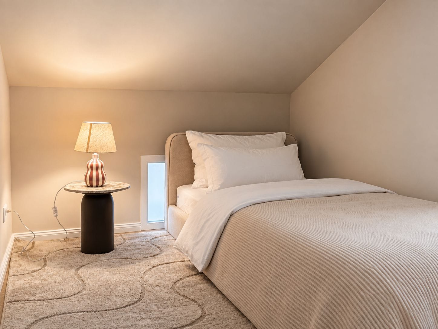 Ein Schlafzimmer mit einem Bett, einem Nachttisch mit Lampe und Teppichboden.