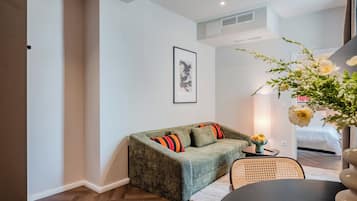 Un salon accueillant avec un canapé vert, une œuvre d’art encadrée et un vase rempli de fleurs.