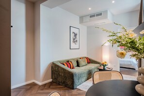 Un salon accueillant avec un canapé vert, une œuvre d’art encadrée et un vase rempli de fleurs.