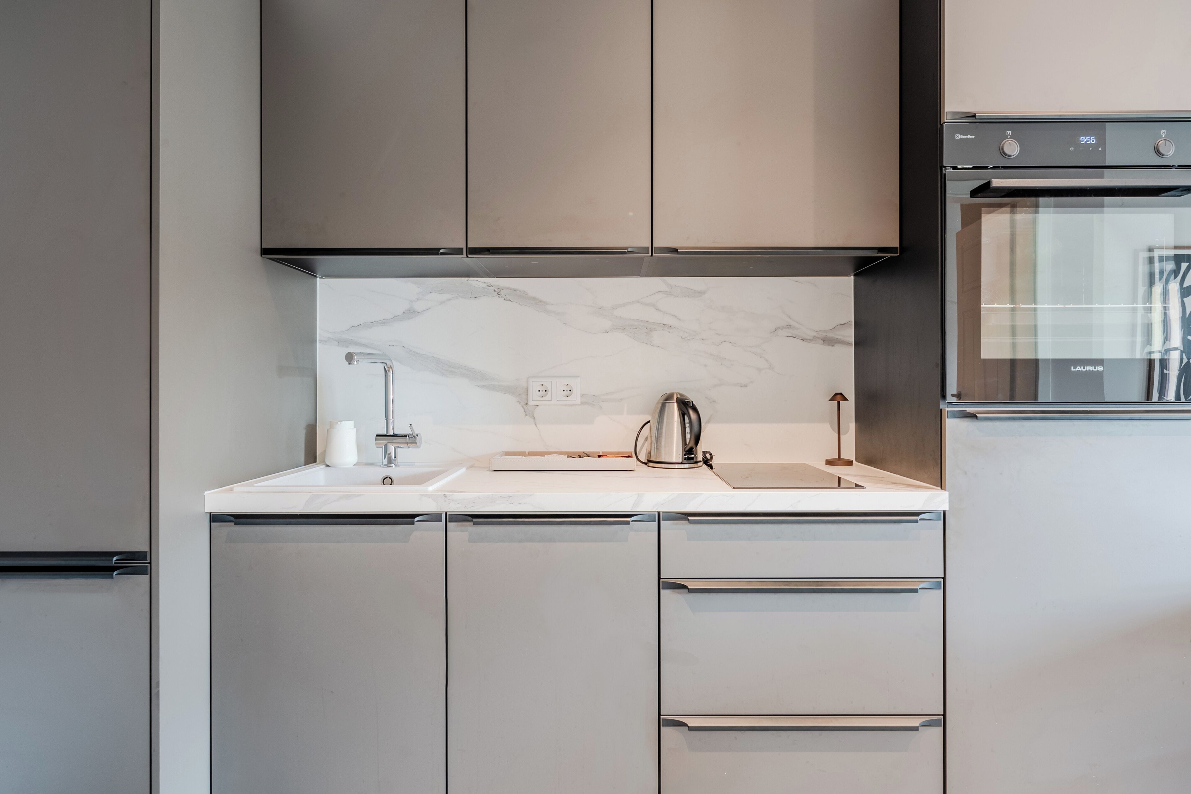 Une cuisine moderne avec des meubles gris, un pare-feu en marbre et des appareils électroménagers en acier inoxydable.