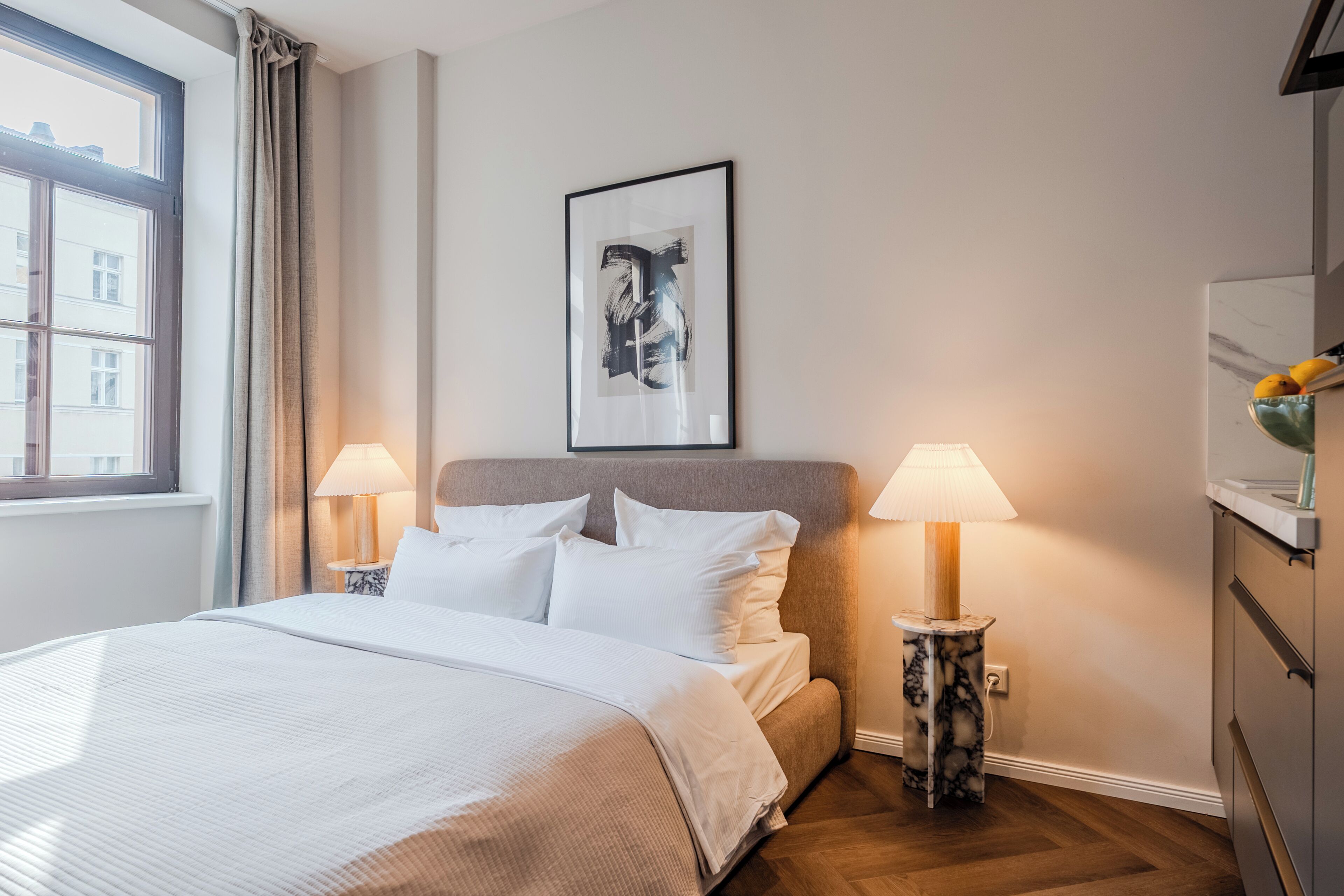 Habitación de hotel con cama, dos lámparas de noche, un cuadro en la pared y una ventana con cortinas.