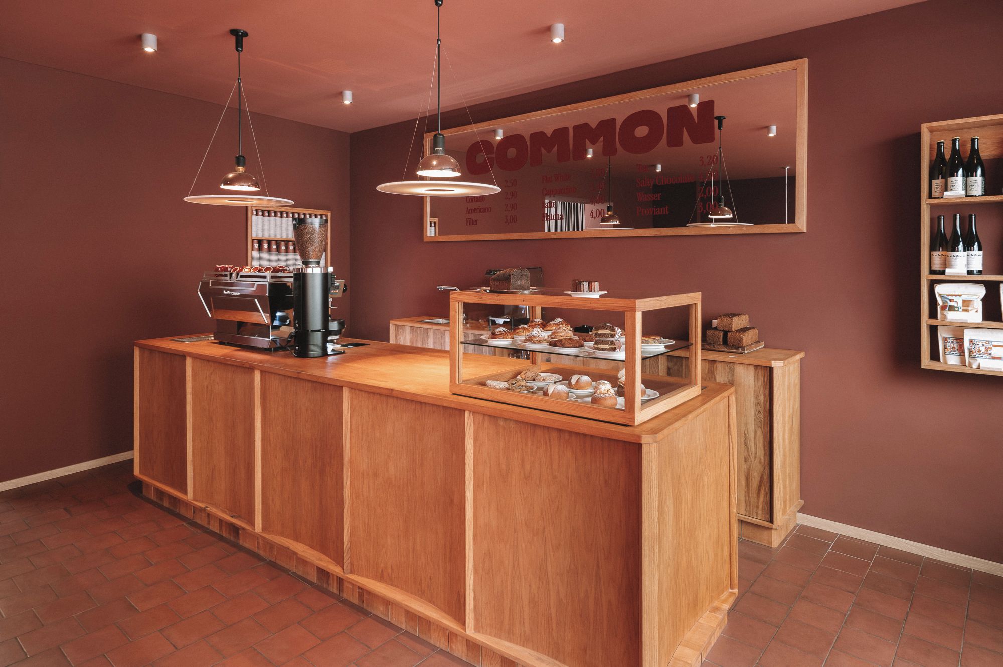 A café counter with a coffee machine, a menu board, and a display case with pastries.