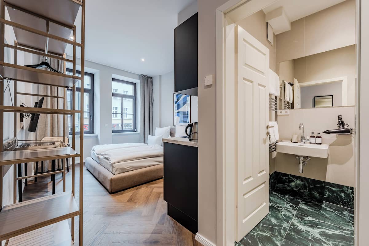 Una habitación de hotel moderna con cama, escritorio, armario, baño con lavabo y espejo, y vista a la ciudad.