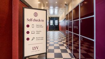 A hotel self-check-in area with numbered lockers and a sign detailing the check-in process.