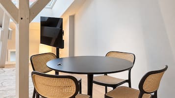 A modern dining area with a round table and four chairs, a flat-screen TV mounted on the wall, and a skylight above.