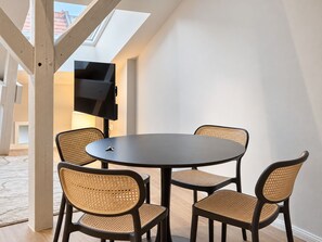 Un espace repas moderne avec une table ronde et quatre chaises, un téléviseur à écran plat fixé au mur et une lucarne au-dessus.