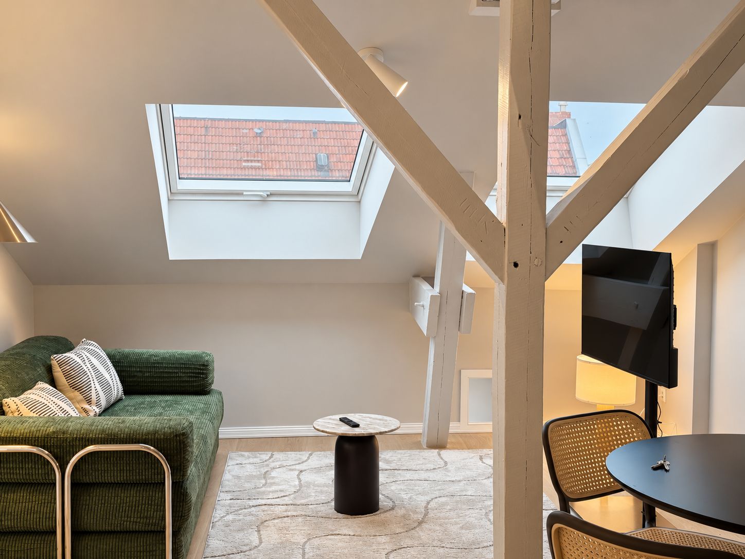 Une chambre de style loft moderne, dotée d’une lucarne, d’un canapé vert, d’une table basse ronde et d’un téléviseur fixé au mur.