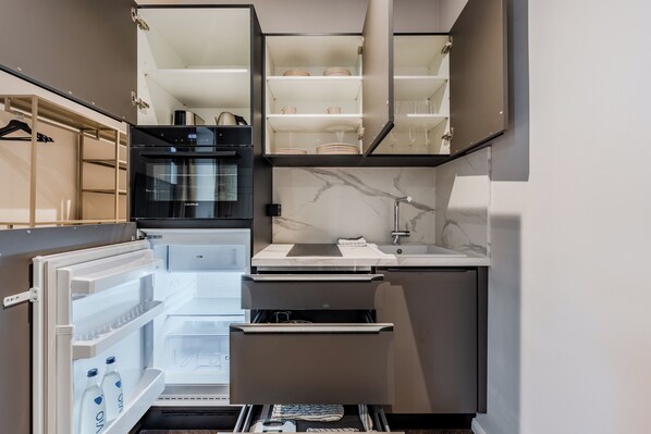 Una cocina compacta con refrigerador integrado, microondas y lavamanos.