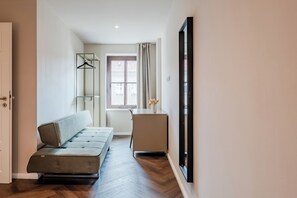 Un couloir avec un canapé, une petite table sur laquelle se trouve un vase, et une porte.