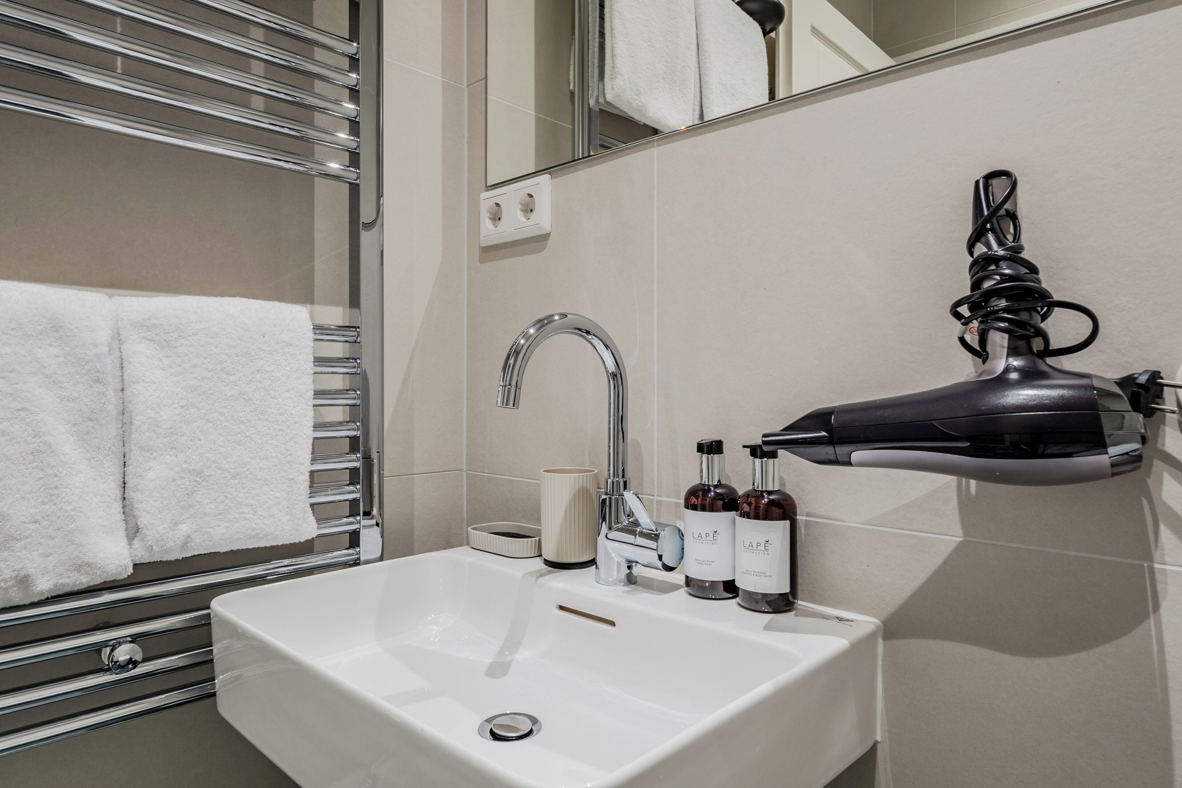 A bathroom with a white sink, a mirror, a towel rack, and two bottles of shampoo.