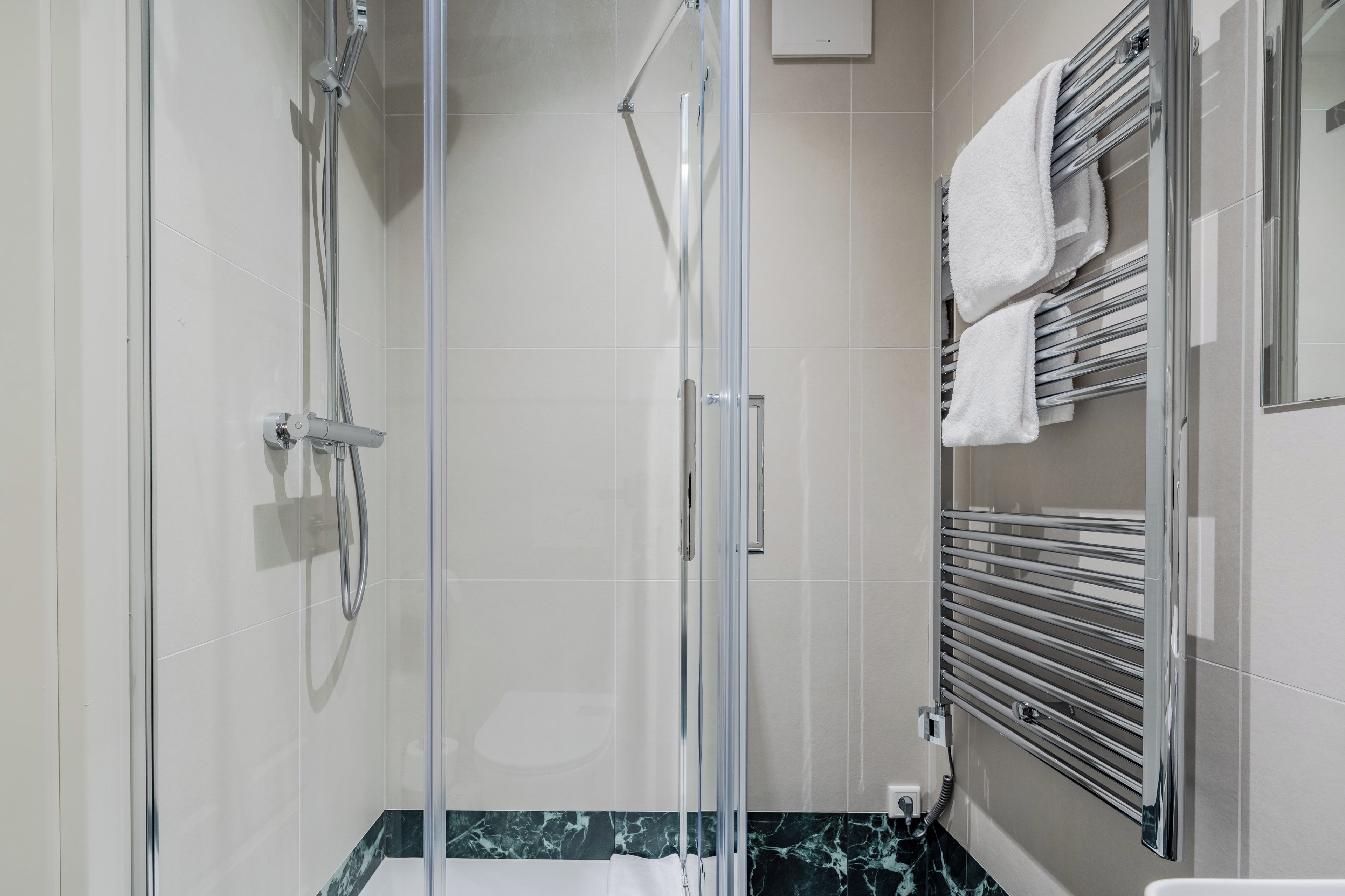Une salle de bain moderne dotée d’une douche à parois de verre, d’un comptoir en marbre et d’un porte-serviettes avec plusieurs serviettes.