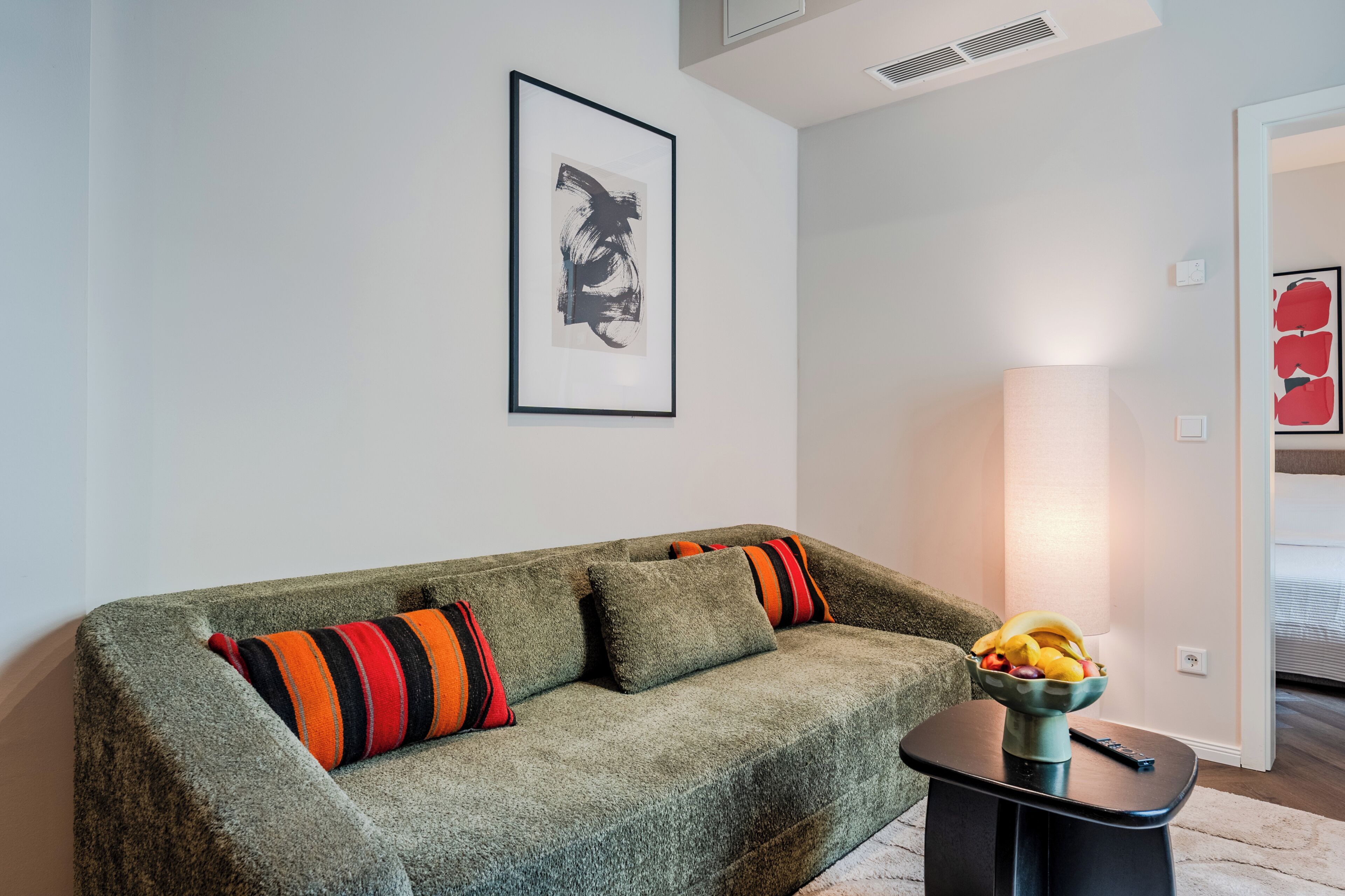 Una sala moderna con un sofá gris, un cuadro abstracto enmarcado y un frutero sobre una mesita de noche.