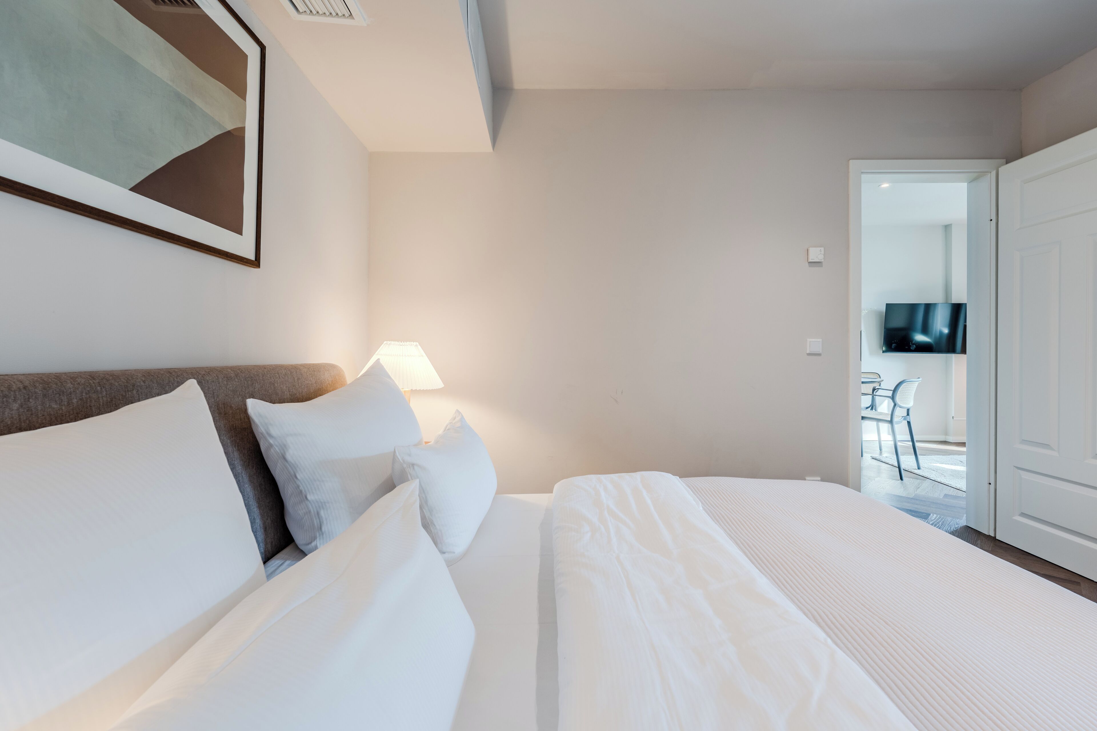Ein Hotelzimmer mit Bett, Kissen, einer Lampe, einem Fernseher und einer Tür, die auf einen Balkon führt.