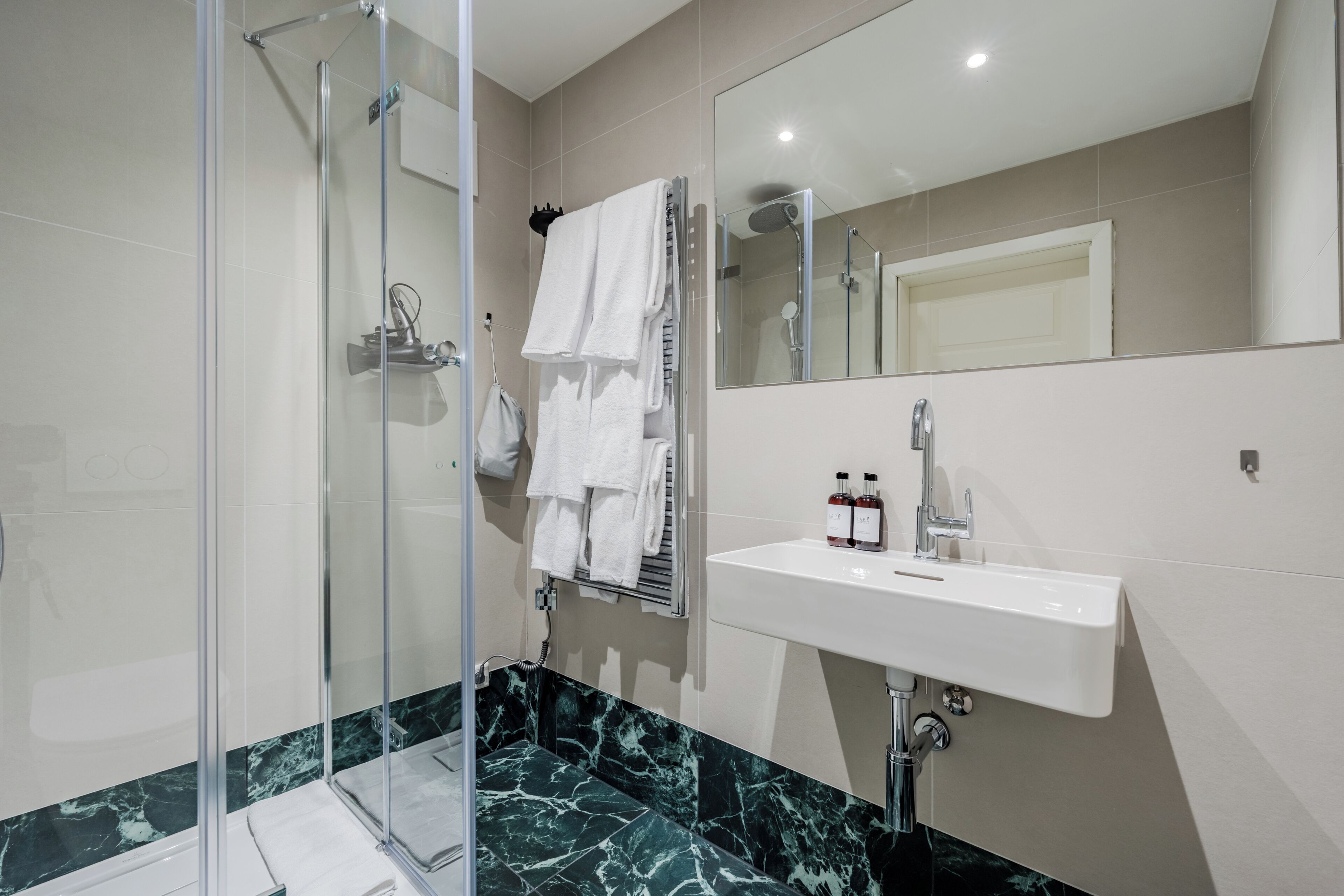 Un baño moderno con cabina de ducha de vidrio, un lavamanos blanco y suelo de baldosas de mármol.