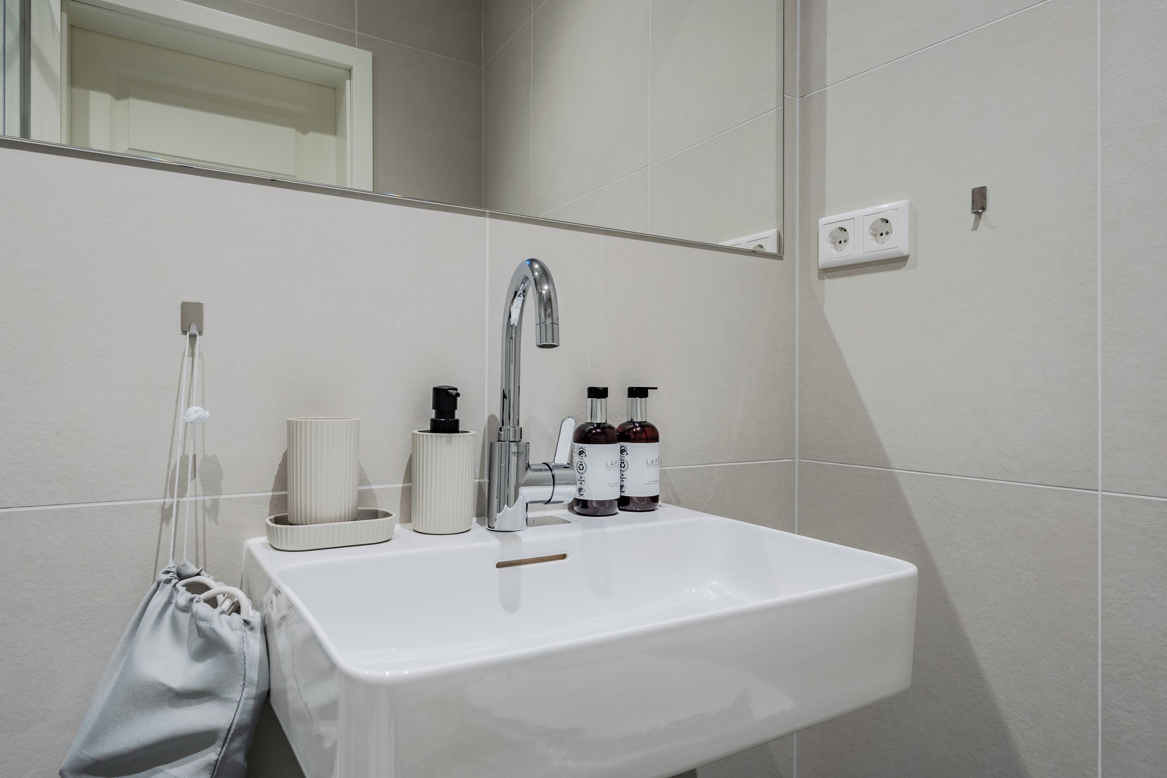Une salle de bain avec un lavabo blanc, un miroir et deux bouteilles de la marque L'APOTHEQUE.